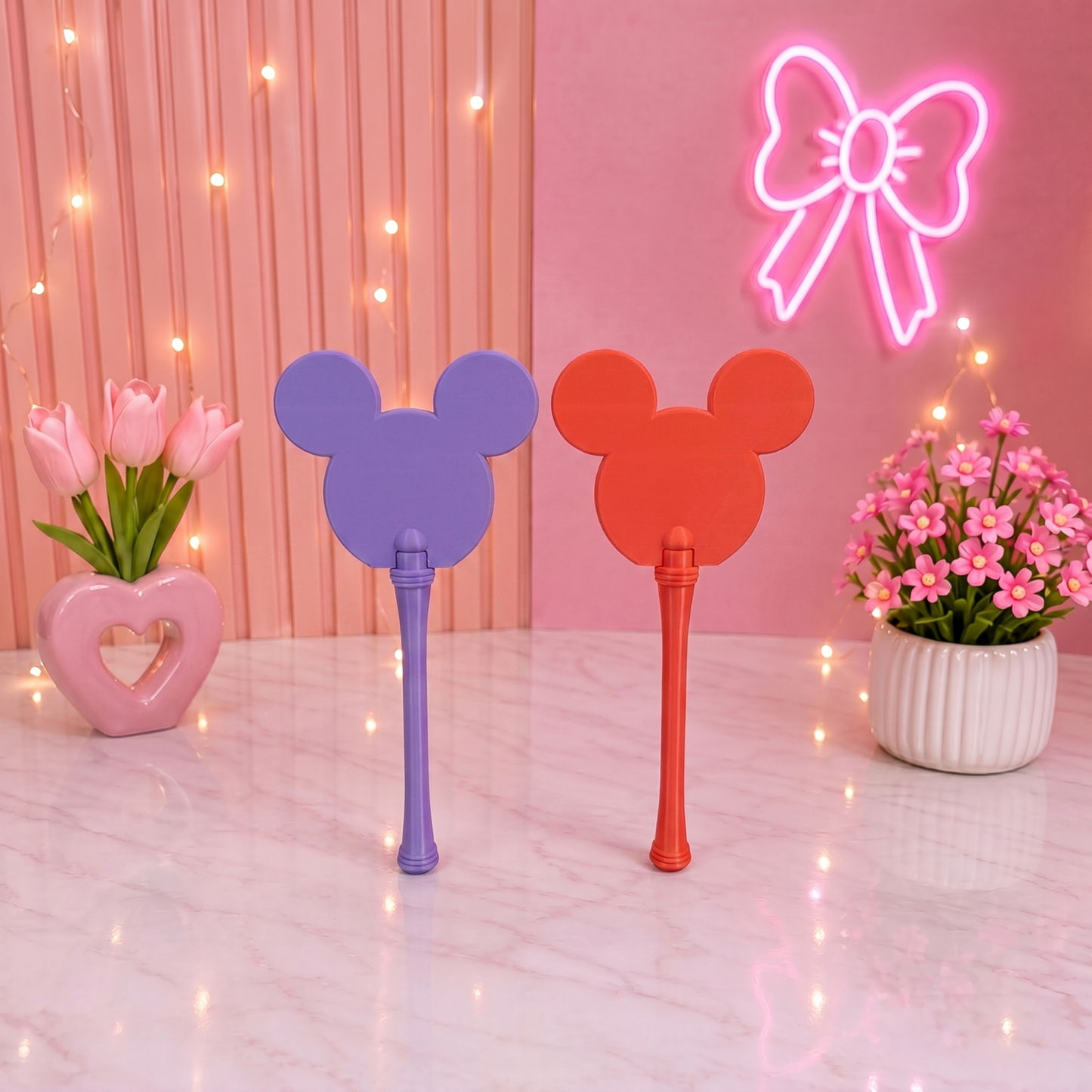 Two colorful fans with Mickey Mouse ears on a pink background with neon bow and flowers.